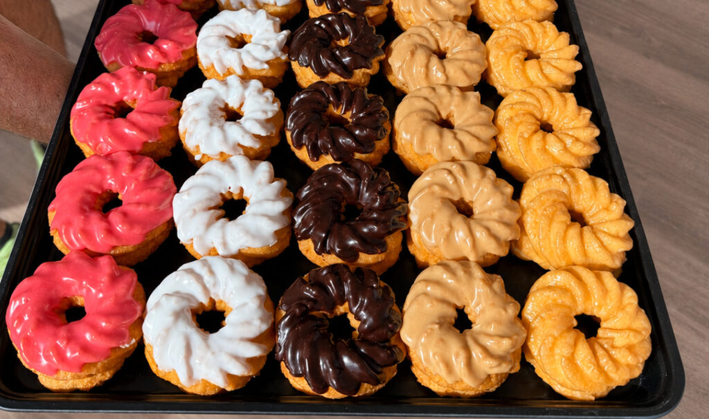 A tray of cruellers with different colored frosting on them.